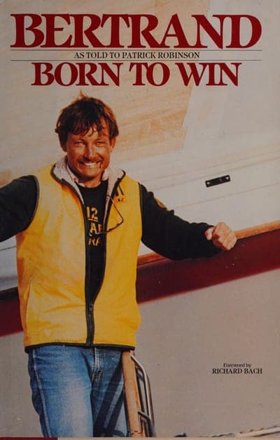 A photographic jacket of a windblown, smiling man in a yellow sailing vest and black jacket standing at the rail of a racing yacht, with 'BERTRAND' in large red serif capitals at top, 'AS TOLD TO PATRICK ROBINSON' in a thin line beneath it, 'BORN TO WIN' in red serif below that, and 'Foreword by RICHARD BACH' in white at lower right.