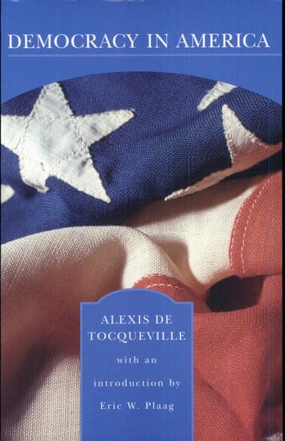 A Barnes & Noble Classics edition of Democracy in America by Alexis de Tocqueville — a folded American flag against a blue ground, "DEMOCRACY IN AMERICA" in white serif type at top and the author's name and introducer's name in a scalloped panel at the bottom.