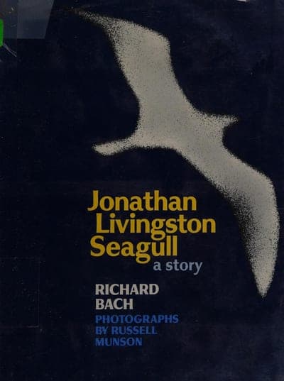 A dark navy hardcover jacket with a black-and-white photograph of a seagull in flight filling the upper two-thirds, the title 'Jonathan Livingston Seagull' in yellow-gold serif type below it, 'a story' in pale blue beneath that, and 'RICHARD BACH' in white capitals with 'PHOTOGRAPHS BY RUSSELL MUNSON' in blue capitals at the foot.