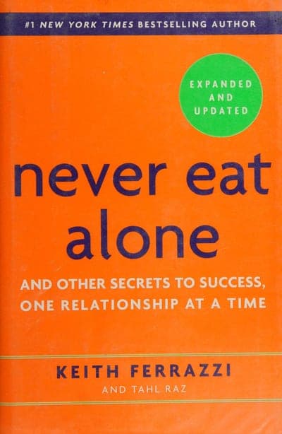The Crown Business expanded-and-updated paperback of Never Eat Alone — a bright orange field with the title set in oversized navy lowercase script, a green 'EXPANDED AND UPDATED' seal at upper right, a '#1 New York Times Bestselling Author' band across the top, and the authors' names in bold navy caps at the bottom.