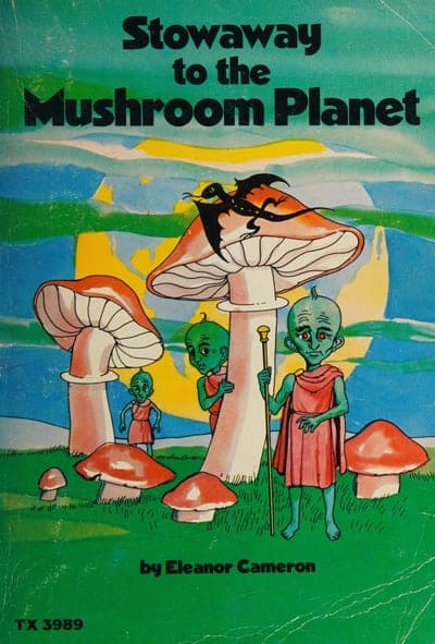 A Scholastic Book Services paperback of Stowaway to the Mushroom Planet — a teal-and-blue painted sky over a cluster of tall orange-and-white mushroom-cap towers, two green-skinned Mushroom People and a bat-winged creature perched atop the tallest cap, the title in bold black lettering across the top, 'by Eleanor Cameron' in white at the bottom, and the order code 'TX 3989' printed at lower left.