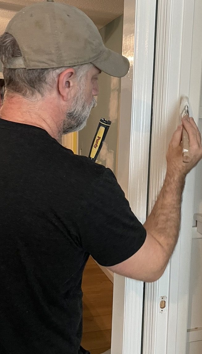 David Clark, wearing a ball cap, brushing white paint onto a door frame
